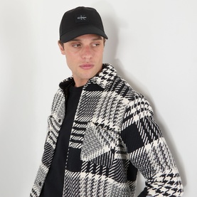 Model with Calvin Klein Rubber Logo Baseball Cap in black, featuring rubber monogram logo badge, styled with black hoodie and houndstooth overshirt