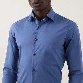 Model wearing Calvin Klein The Poplin Slim Fit Shirt in blue, slim fit with dark buttons, pointed collar and long sleeves visible.