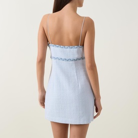 Model wearing pale blue linen mini dress with spaghetti straps, floral trim detail at back, and fitted silhouette, shown from behind.