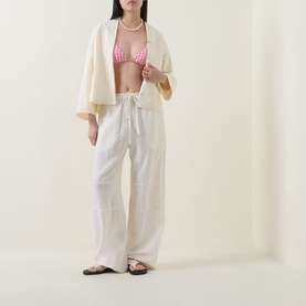 Model wearing Seafolly Begonia Pink bikini top, styled with cream wide-leg trousers, open shirt, and black sandals.