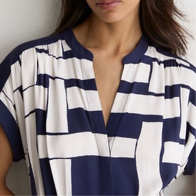 Model wearing navy and white geometric print V-neck top with short sleeves and draped front detail
