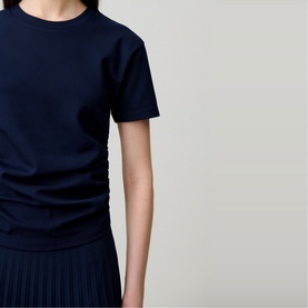 Model wearing Claude Pierlot blue short-sleeve crew-neck top with ruched side detail, styled with a pleated skirt.