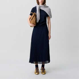 Model wearing Claude Pierlot blue pleated midi dress with short sleeves, styled with grey scarf, tan bag, and leopard-print trainers.