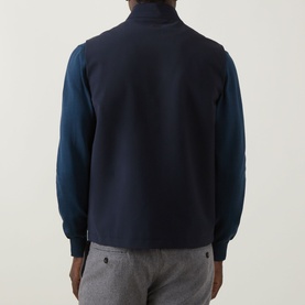Model wearing Eton Lana Technical Gilet in navy blue, high neck, sleeveless, styled with a navy sweatshirt and grey trousers, rear view.