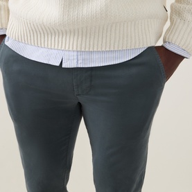Model wearing Hugo Boss Orange Open Green cotton chino trousers, styled with a cream knit sweater and blue striped shirt.