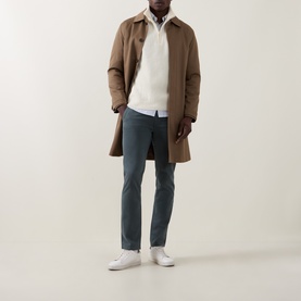 Model wearing Hugo Boss Orange Open Green chino trousers styled with a camel overcoat, cream knit, and white trainers.