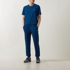 Model wearing teal blue joggers styled with a matching teal crew-neck tee and grey trainers.