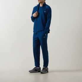 Model wearing blue zip-up track jacket and matching joggers with white detailing, styled with a blue T-shirt and grey trainers