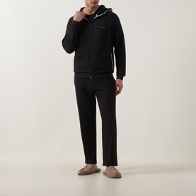 Model wearing Hugo Boss black zip-up hooded lounge top with matching black joggers and beige slippers.