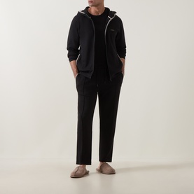 Model wearing Hugo Boss black zip-through hoodie with white trim detail, styled with black tapered trousers and grey mule slippers.