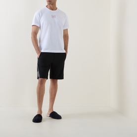 Model wearing Hugo Laze Logo Lounge T-Shirt in white with black logo shorts and navy slippers.