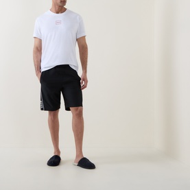 Model wearing Hugo Laze Logo Lounge T-Shirt in white with black logo shorts and navy slippers.