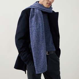 Model with John Smedley Knit Oblong Scarf in dark blue cashmere-wool blend, styled over a navy wool coat with black trousers.
