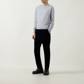 Model wearing John Smedley Lundy Extra Fine Knit Sweater in light grey with black trousers and black chunky loafers.