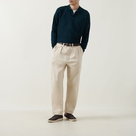 Model wearing John Smedley Belper Extra Fine Knit Polo Shirt in dark green, styled with cream wide-leg trousers and dark loafers.