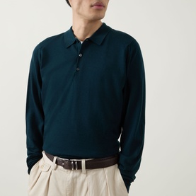 Model wearing John Smedley Belper Extra Fine Knit Polo Shirt in Dark Green, long sleeves, flat knit collar, styled with stone trousers and brown belt.