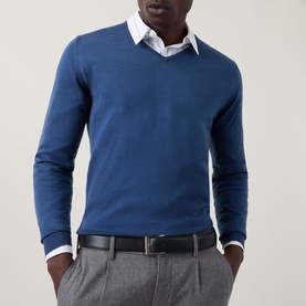 Model wearing John Smedley Blenheim Extra Fine Knit Sweater in Teal Firth, V-neck wool knit, styled with white shirt, grey trousers and black belt.