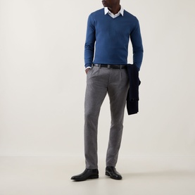 Model wearing John Smedley Blenheim Extra Fine Knit Sweater in Teal Firth, V-neck, styled with white shirt, grey trousers and black shoes.