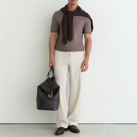 Model carrying large black leather tote bag with top handles; styled with taupe T-shirt, cream wide-leg trousers and dark brown scarf