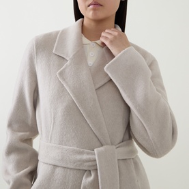 Model wearing Hugo Boss Open White wool-blend belted coat with wide lapels, styled with a white polo shirt, close-up detail view.