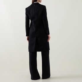 Model wearing Hugo Boss black wool coat, rear view, styled with wide-leg black trousers. Longline silhouette with structured shoulders.