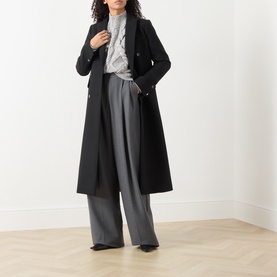 Model wearing Hugo Boss knitwear in grey, styled with a black longline coat and wide-leg grey trousers.