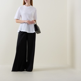 Model wearing Hugo Boss white cotton T-shirt with relaxed fit, styled with wide-leg black trousers and small dark shoulder bag.