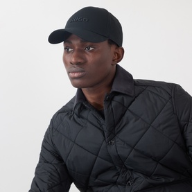 Model with Hugo Jude Logo Baseball Cap in black, curved visor with embroidered logo, styled with black quilted jacket