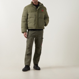 Model wearing Hugo Open Green puffer casual jacket with red logo detail, styled with matching cargo trousers and black trainers.
