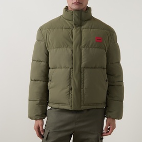 Model wearing Hugo Casual Jacket in Open Green, quilted puffer style with funnel neck, red logo patch, paired with khaki trousers