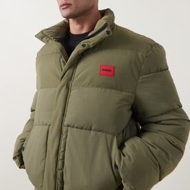 Model wearing Hugo casual jacket in Open Green, quilted puffer style with red logo patch and funnel neck