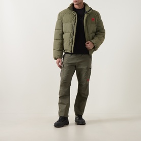Model wearing Hugo Open Green casual puffer jacket with matching cargo trousers, black crew-neck jumper and black trainers.