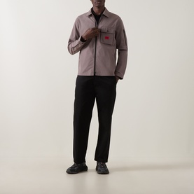Model wearing taupe zip-through overshirt with red chest pocket detail, styled with black trousers and black shoes