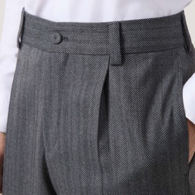 Model wearing Hugo Suit Trouser in dark grey herringbone fabric, showing pleated front, button waistband and side pockets.