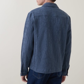 Model wearing Paul Smith blue cotton casual jacket, shown from behind, styled with dark denim jeans. Textured crinkle fabric detail visible.