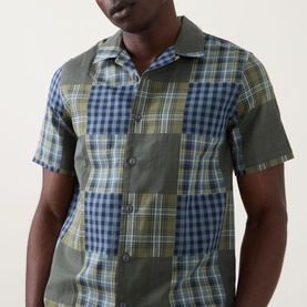 Model wearing Paul Smith Patchwork Check Shirt in green and navy, camp collar, short sleeves, patchwork check pattern visible at chest.
