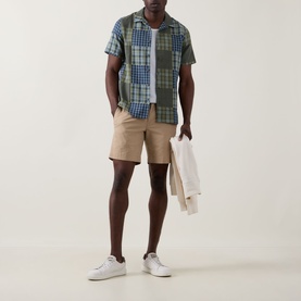 Model wearing Paul Smith Patchwork Check Shirt in green/navy with beige chino shorts and white trainers, holding a cream jacket.