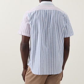 Model wearing Paul Smith white striped casual shirt, short sleeves, mixed stripe pattern, styled with tan trousers. Back view.