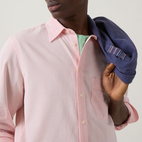 Model wearing Paul Smith pink stripe casual shirt, styled with mint green layer beneath; carrying navy cap over shoulder.
