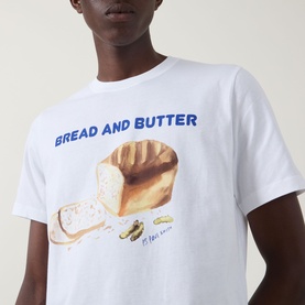 Model wearing Paul Smith Bread & Butter Logo T-Shirt in white, featuring bold bread and butter graphic print with blue text on chest.