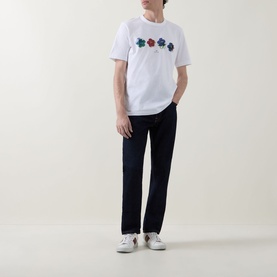 Model wearing Paul Smith white cotton crew neck T-shirt with multicoloured floral print, styled with dark navy trousers and white trainers.