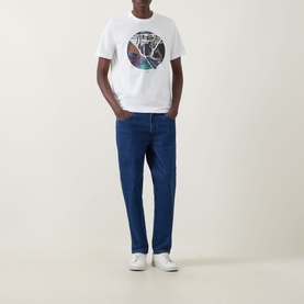 Model wearing Paul Smith Graphic Logo T-Shirt in white with circular graphic print, styled with mid-blue straight-leg jeans and white trainers.