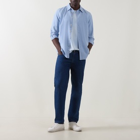 Model wearing Paul Smith Logo Faded T-Shirt in blue, styled with a light blue overshirt, dark navy jeans and white trainers.