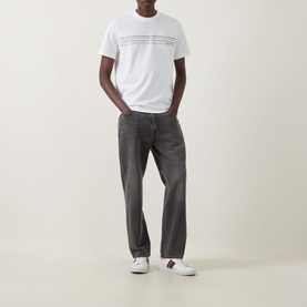 Model wearing Paul Smith Stripe Logo T-Shirt in white with stripe graphic detail, styled with grey jeans and white trainers.