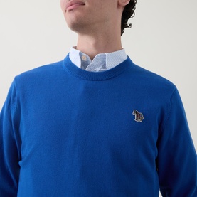 Model wearing Paul Smith Zebra Badge Logo Sweater in blue cotton, crew neck with embroidered zebra badge, styled over light blue collared shirt.