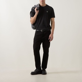 Model wearing Paul Smith black crew neck T-shirt with black trousers and belt, carrying dark bag, paired with black leather shoes.