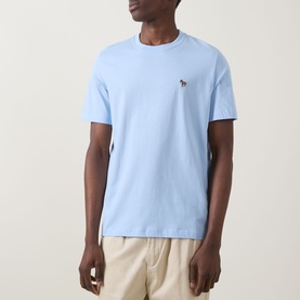 Model wearing Paul Smith blue crew neck T-shirt with zebra logo chest badge, styled with cream trousers