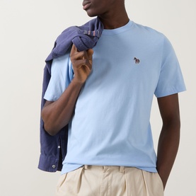 Model wearing Paul Smith blue crew neck T-shirt with embroidered zebra logo, styled with navy shirt draped over shoulder and beige trousers