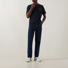 Model wearing Paul Smith blue crew neck T-shirt with small chest logo, styled with dark indigo jeans and white trainers.