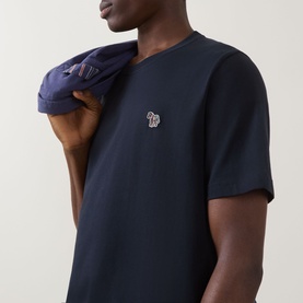 Model wearing Paul Smith blue crew neck T-shirt with zebra logo badge, styled with a navy jacket over the shoulder.